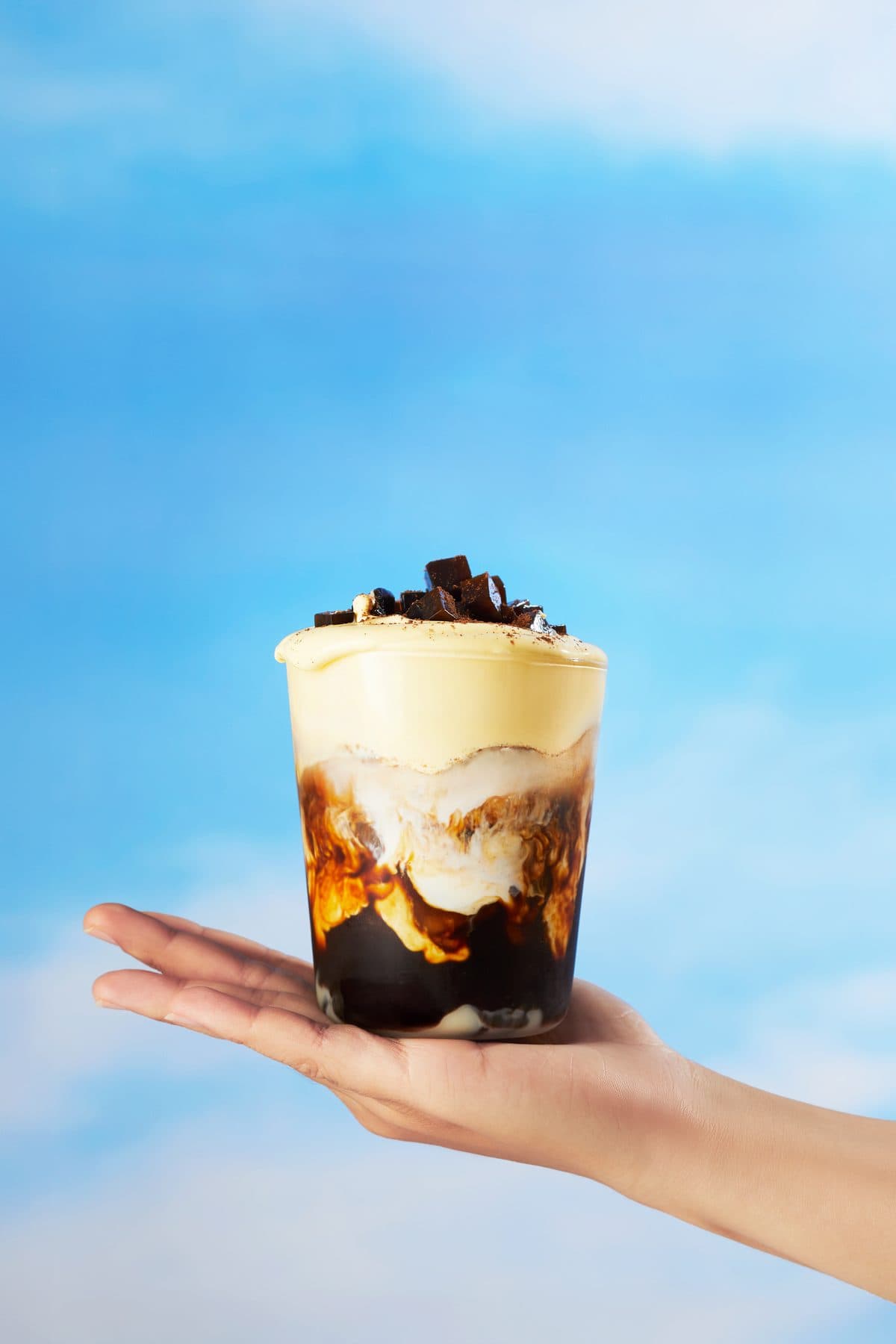 Hand holding a cup of Trạm Egg Coffee layered with rich egg cream over dark brew